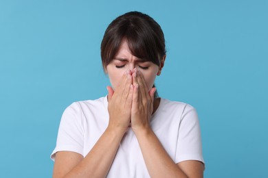 Woman suffering from sinusitis on light blue background