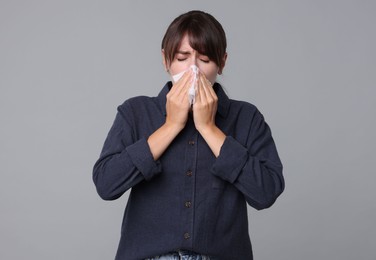 Woman with napkin suffering from sinusitis on grey background