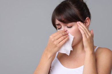 Woman with napkin suffering from sinusitis on grey background. Space for text