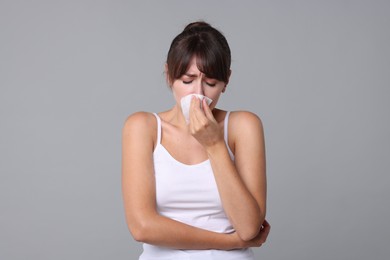 Woman with napkin suffering from sinusitis on grey background