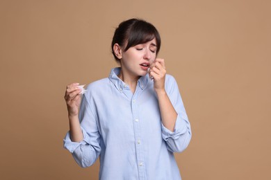 Woman with napkin suffering from sinusitis on beige background