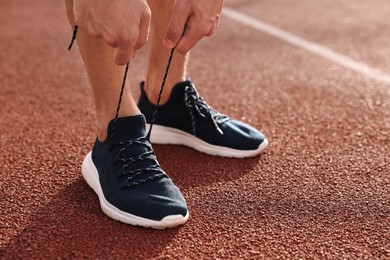 Photo of Man tying shoelace of black sneaker at stadium, closeup. Space for text