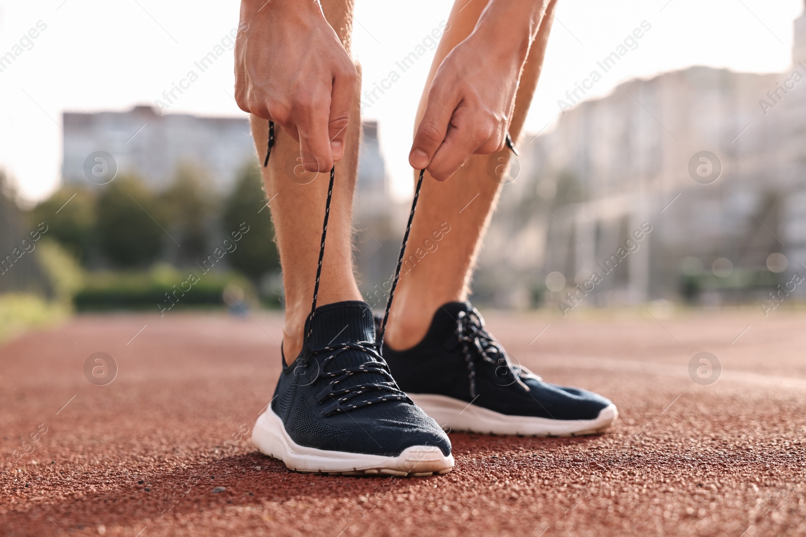 Photo of Man tying shoelace of black sneaker at stadium, closeup