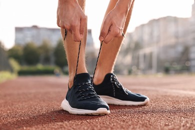 Man tying shoelace of black sneaker at stadium, closeup