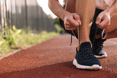 Photo of Man tying shoelace of black sneaker at stadium, closeup. Space for text