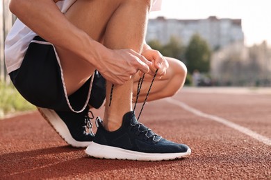 Photo of Man tying shoelace of black sneaker at stadium, closeup. Space for text