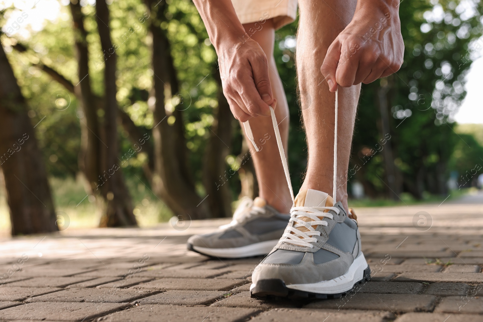 Photo of Man tying shoelace of grey sneaker outdoors, closeup. Space for text