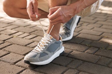 Photo of Man tying shoelace of grey sneaker outdoors, closeup