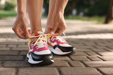 Photo of Woman tying shoelace of sneaker outdoors, closeup. Space for text