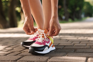 Photo of Woman tying shoelace of sneaker outdoors, closeup