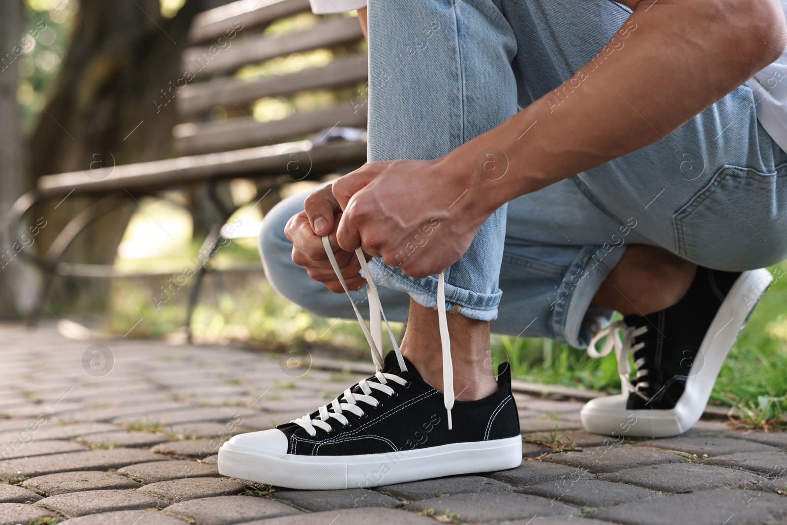 Photo of Man tying shoelace of black sneaker outdoors, closeup