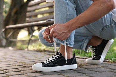 Man tying shoelace of black sneaker outdoors, closeup