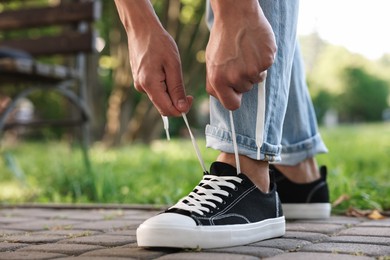 Photo of Man tying shoelace of black sneaker outdoors, closeup. Space for text