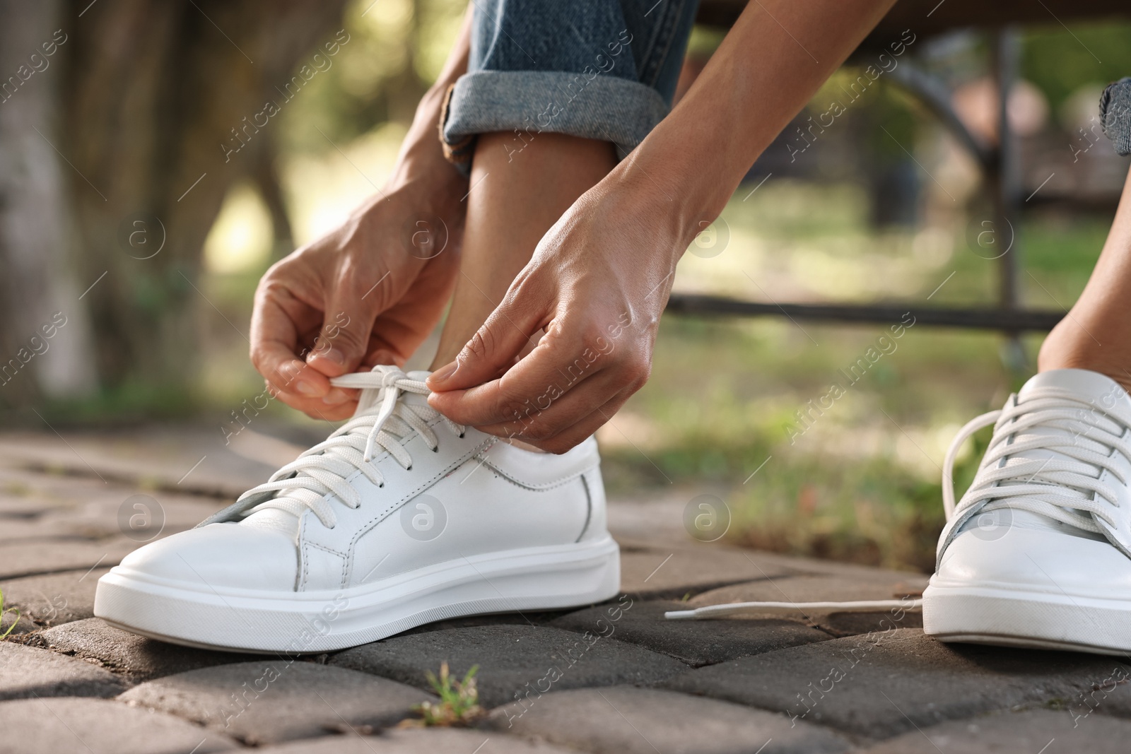 Photo of Woman tying shoelace of white sneaker outdoors, closeup