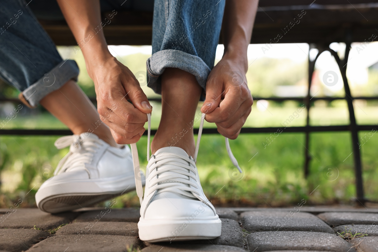 Photo of Woman tying shoelace of white sneaker outdoors, closeup. Space for text