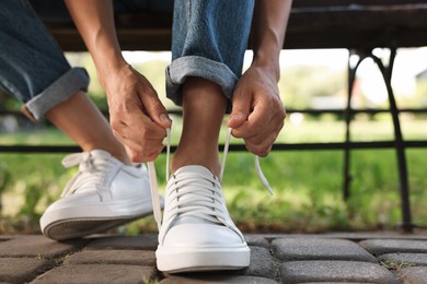 Photo of Woman tying shoelace of white sneaker outdoors, closeup. Space for text