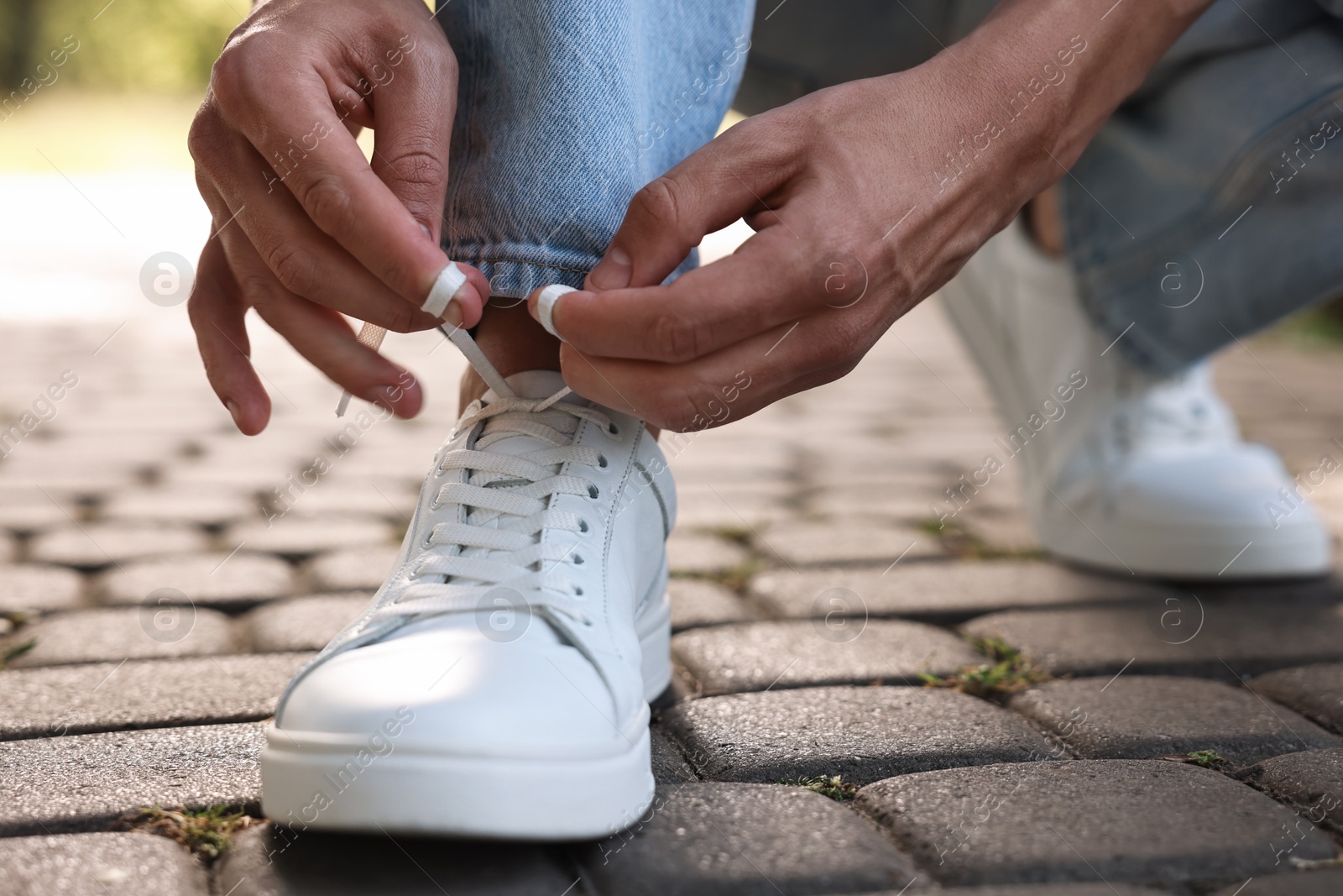 Photo of Man tying shoelace of white sneaker outdoors, closeup