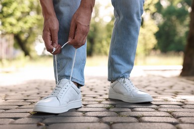 Photo of Man tying shoelace of white sneaker outdoors, closeup