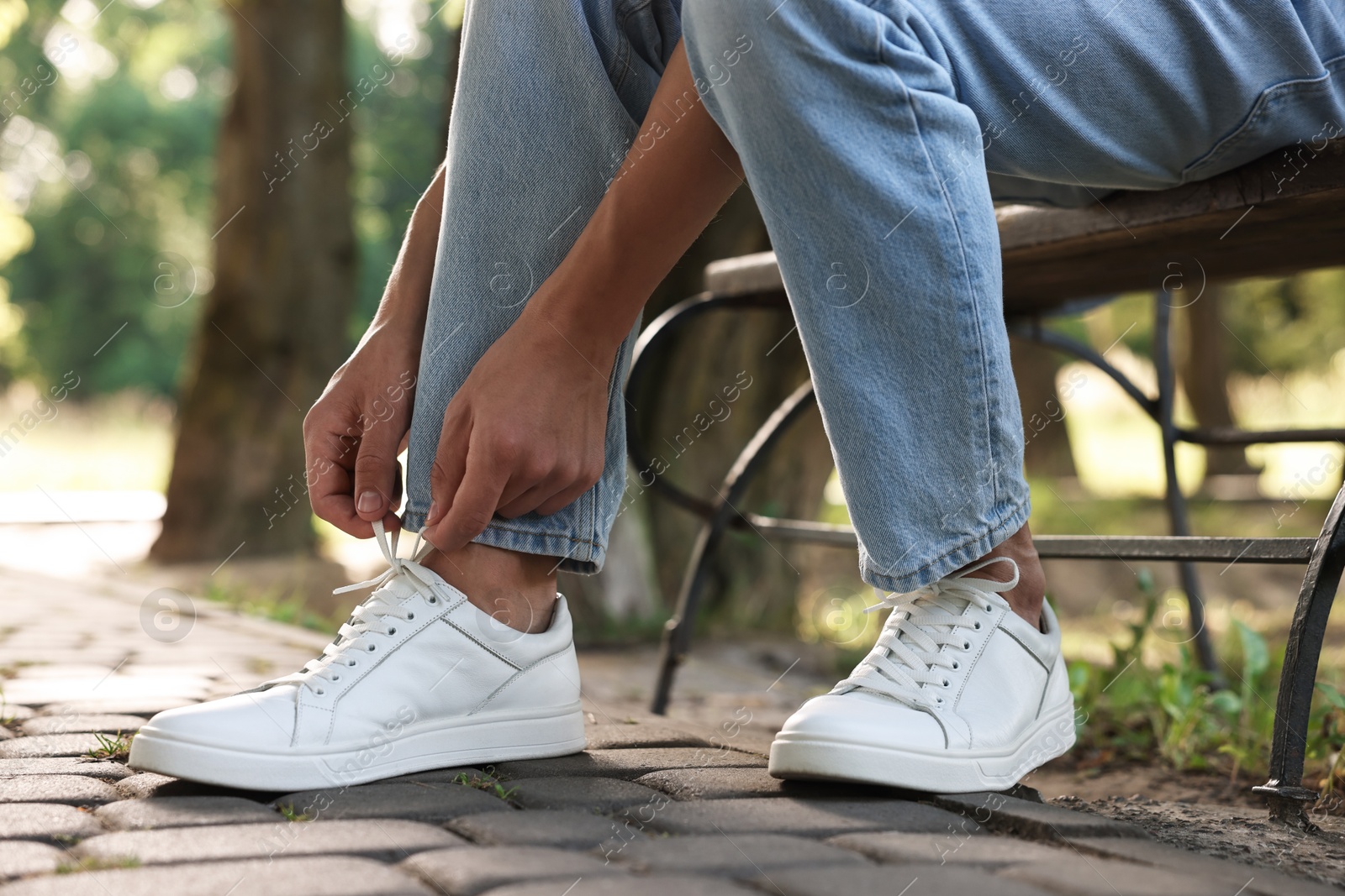 Photo of Man tying shoelace of white sneaker outdoors, closeup