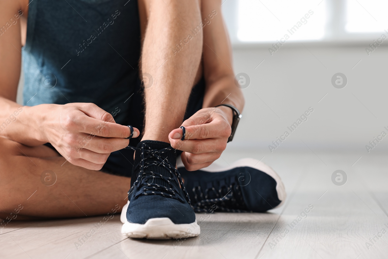 Photo of Man tying shoelace of sneaker indoors, closeup. Space for text