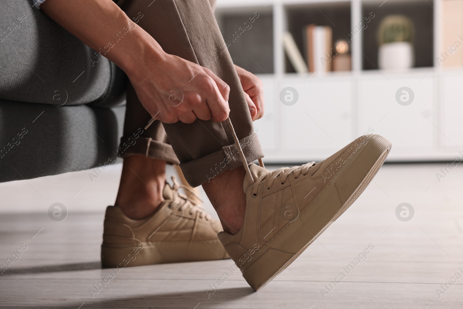 Photo of Man tying shoelace of sneaker on sofa indoors, closeup