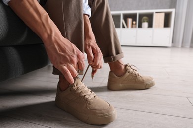 Man tying shoelace of sneaker on sofa indoors, closeup