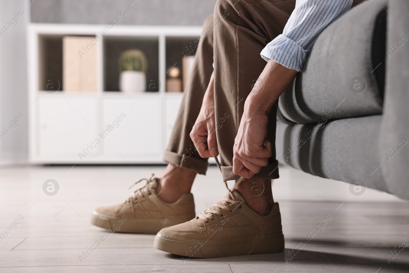 Photo of Man tying shoelace of sneaker on sofa indoors, closeup