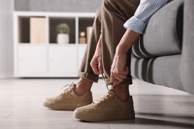 Photo of Man tying shoelace of sneaker on sofa indoors, closeup