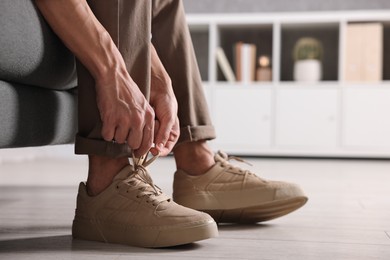 Photo of Man tying shoelace of sneaker on sofa indoors, closeup