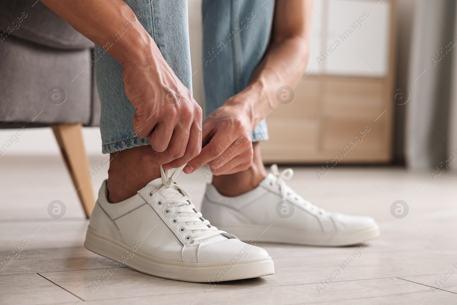 Photo of Man tying shoelace of sneaker indoors, closeup