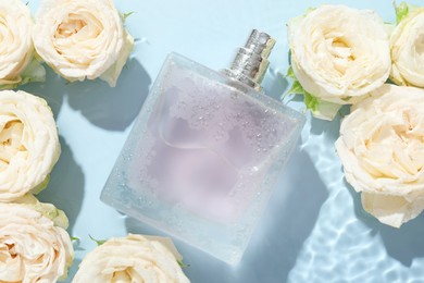 Beautiful rose flowers and perfume bottle in water on light blue background, flat lay