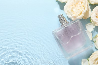 Beautiful rose flowers and perfume bottle in water on light blue background, flat lay. Space for text