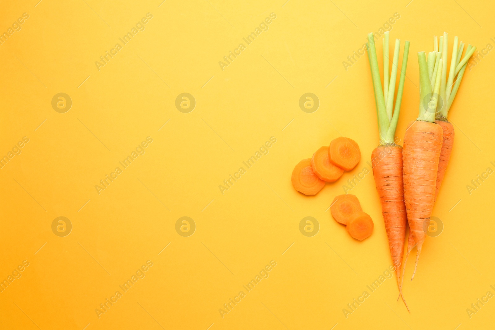 Photo of Whole and cut carrots on yellow background, flat lay. Space for text