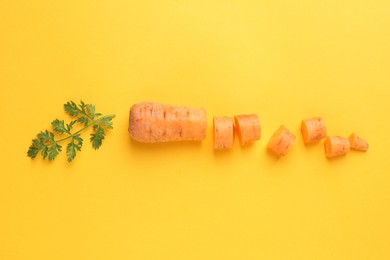 Photo of Pieces of fresh ripe carrot and green leaf on yellow background, flat lay