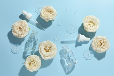 Photo of Beautiful rose flowers, cosmetic bottles, pipettes and drops of serum on light blue background, flat lay