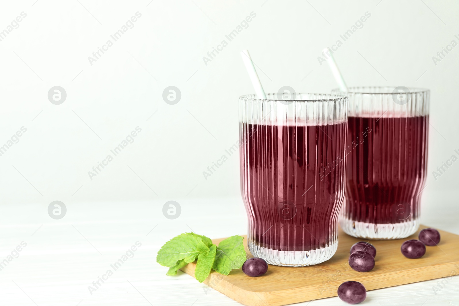 Photo of Delicious acai juice in glasses, berries and mint on white wooden table. Space for text