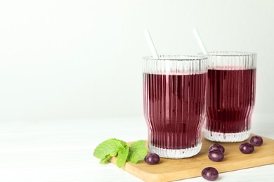 Photo of Delicious acai juice in glasses, berries and mint on white wooden table. Space for text