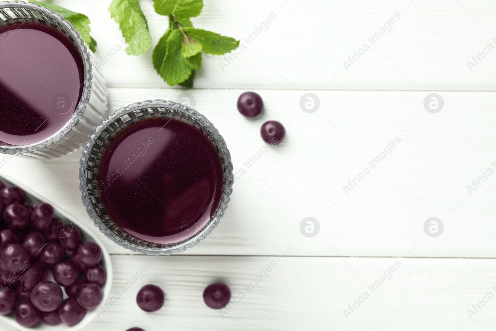 Photo of Delicious acai juice in glasses, berries and mint on white wooden table, flat lay. Space for text