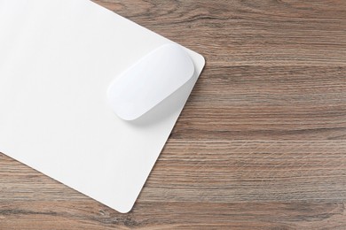 Photo of Computer mouse with mousepad on wooden desk, top view. Space for text