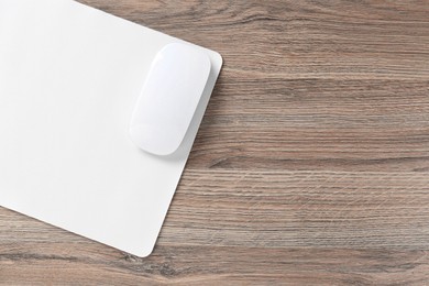 Photo of Computer mouse with mousepad on wooden desk, top view. Space for text