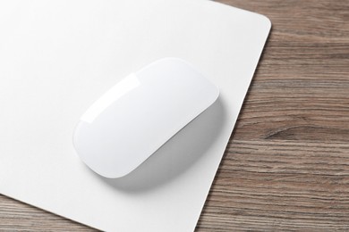 Photo of Computer mouse with mousepad on wooden desk, closeup