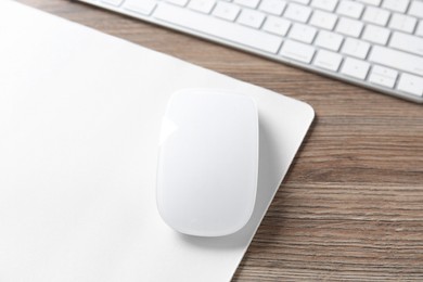 Photo of Computer mouse with mousepad and keyboard on wooden desk, closeup