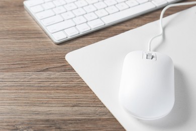 Photo of Computer mouse with mousepad and keyboard on wooden desk, closeup