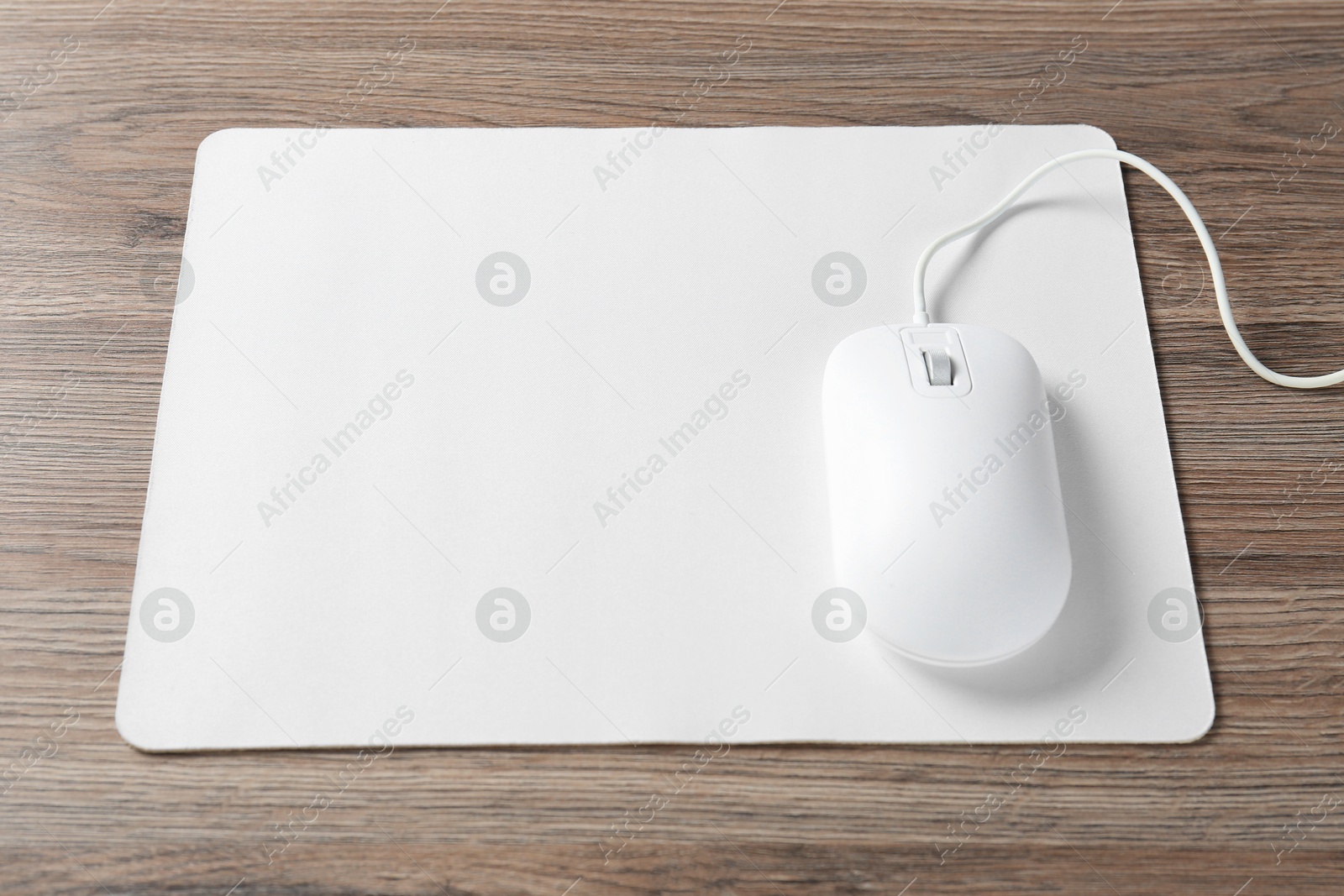 Photo of Computer mouse with mousepad on wooden desk, closeup