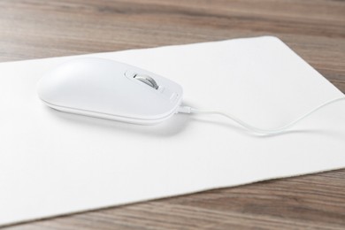 Photo of Computer mouse with mousepad on wooden desk, closeup