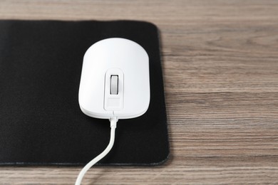 Photo of Computer mouse with mousepad on wooden desk, closeup