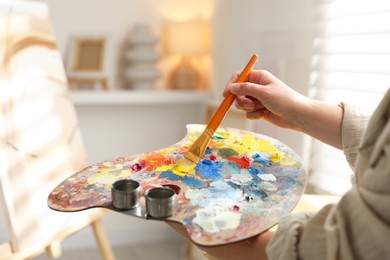 Photo of Woman mixing paints on palette with brush indoors, closeup