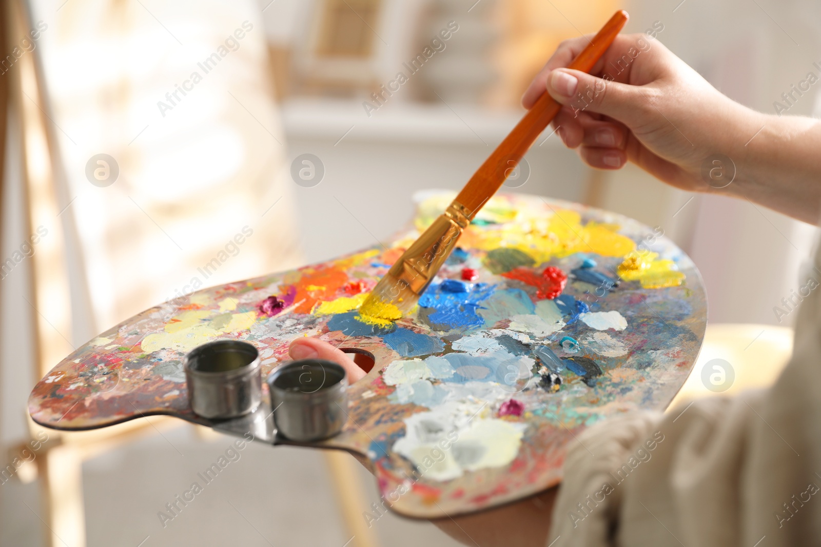 Photo of Woman mixing paints on palette with brush indoors, closeup