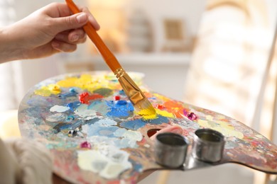 Photo of Woman mixing paints on palette with brush indoors, closeup