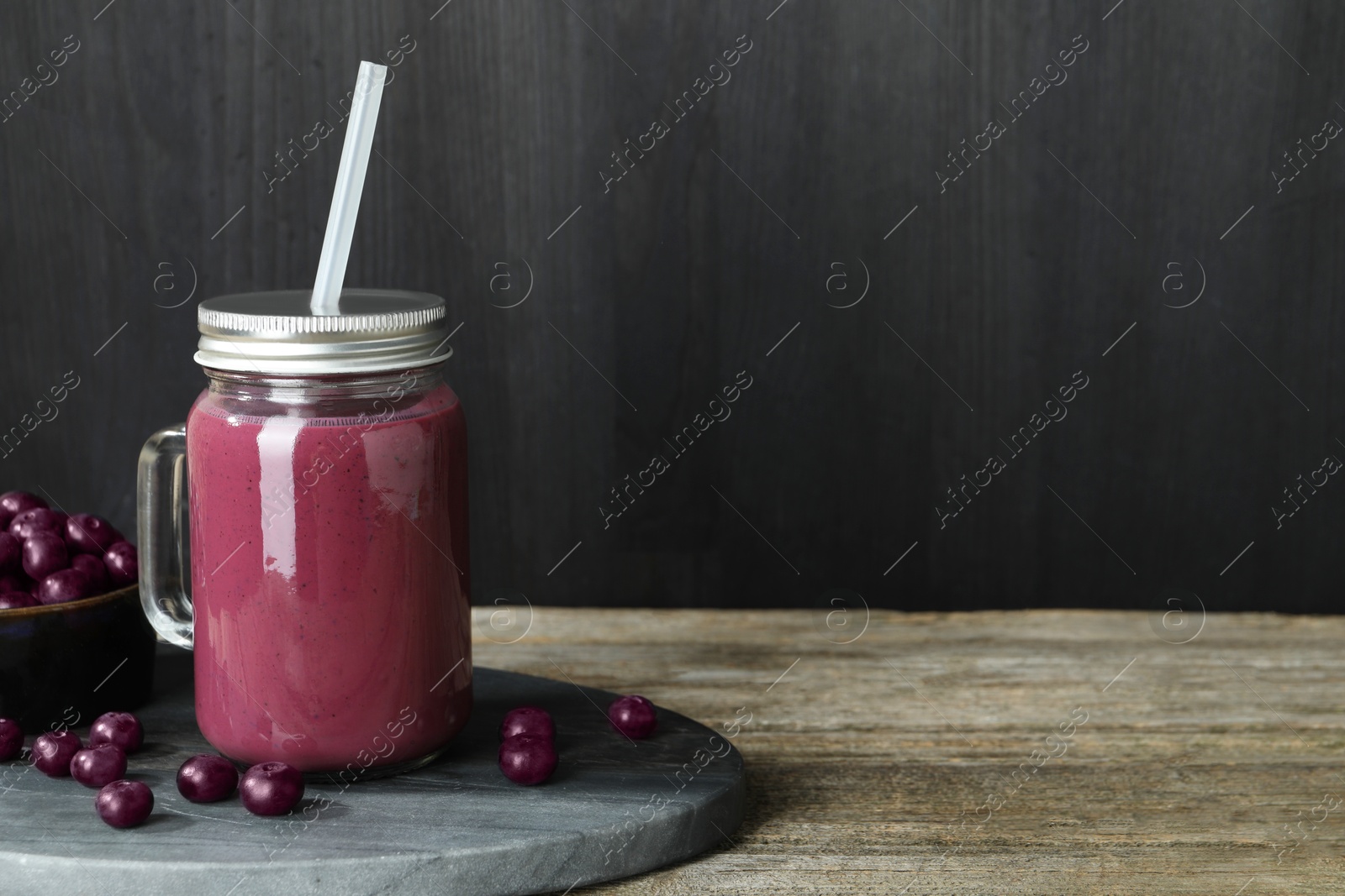 Photo of Tasty fresh acai juice in mason jar and berries on wooden table, space for text